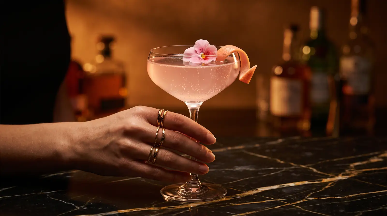 Cóctel rosado en copa coupé con flor comestible sobre barra de mármol